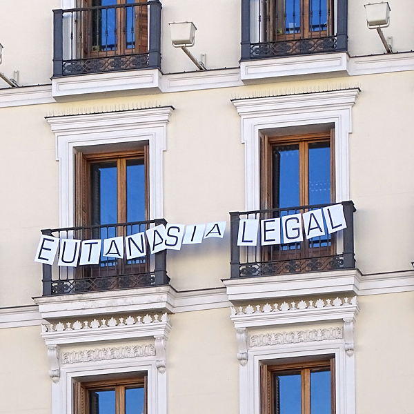 Foto que muestra un cartel que lee 'Eutanasia legal' colgando entre dos balcones